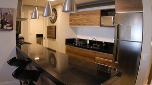 A modern kitchen with stainless steel appliances, wooden cabinets, and pendant lighting. - Gramado me Aptos de Luxo Via Florida (Gramado)