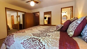 Ein Schlafzimmer mit einem Bett, einem Schreibtisch und einem Stuhl. Es gibt zwei Türen, eine zu einem Badezimmer und eine zu einem Schrank.