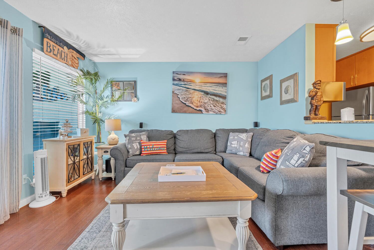 Una sala de estar con un sofá gris, una mesa de centro de madera, un aparador con objetos decorativos y un cuadro de una playa.