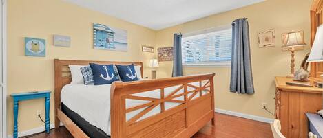 Une chambre à coucher avec un lit en bois, une petite table de chevet, un bureau avec une lampe et des décorations murales sur le thème de la marine.