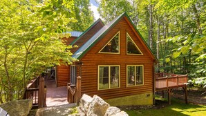 Une cabane en rondins avec un toit végétalisé, une terrasse en bois et un chemin de pierre menant à l’entrée.