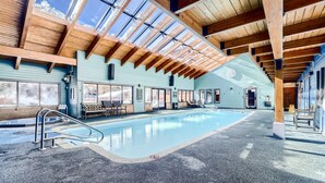 An indoor swimming pool with clear glass ceilings, wooden beams, and seating areas. - Mountainside 523 3 Bedroom Home by RedAwning (Frisco)