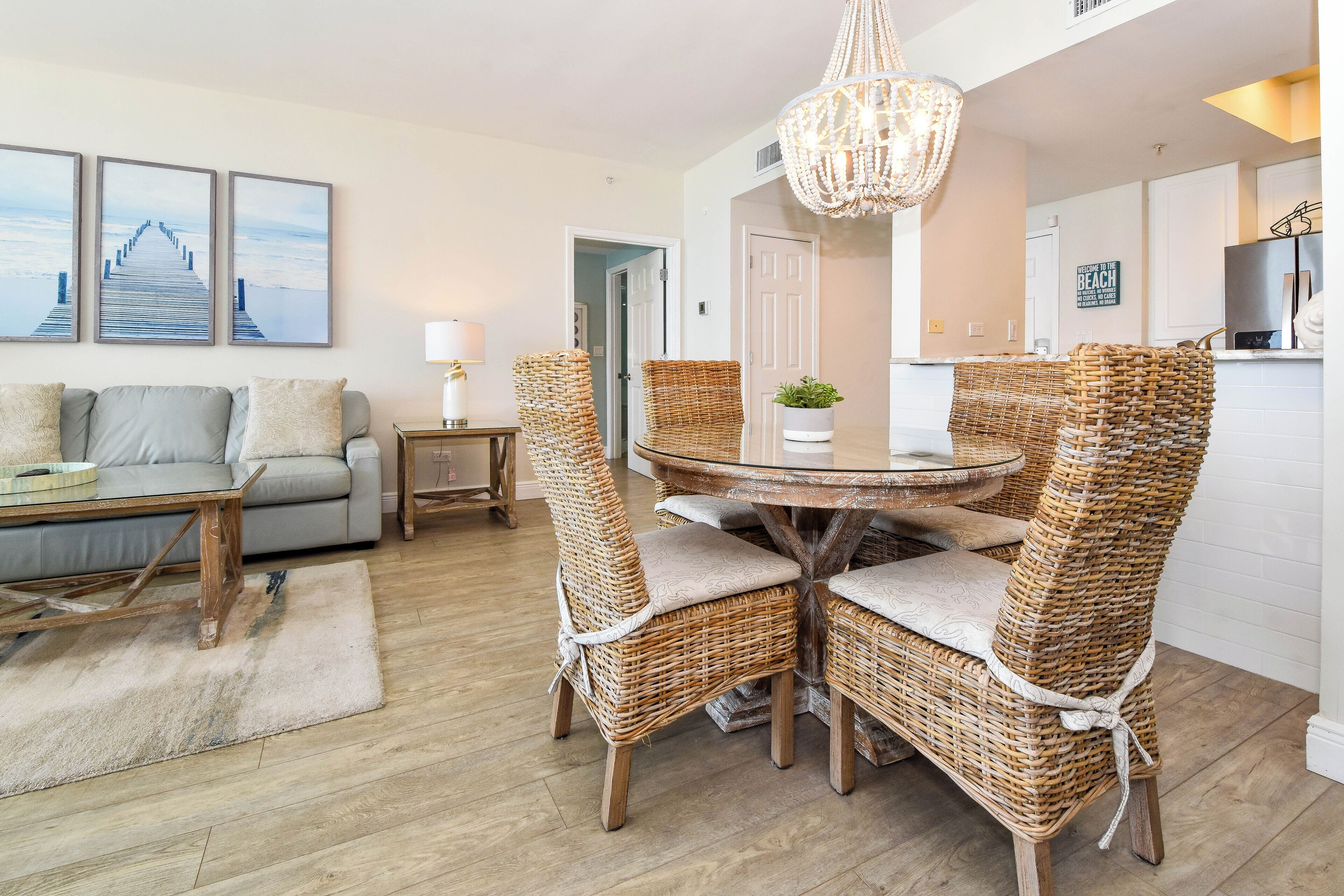 Un salon avec un canapé, une table basse et des fauteuils en osier disposés autour d’une table ronde. Un lustre est suspendu au-dessus de la table.