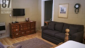 A room with a wooden dresser, a dark brown sofa, a flat-screen TV mounted on the wall, a framed picture, and a clock. - The 87Getaway Cabin #1 (Mountain View)