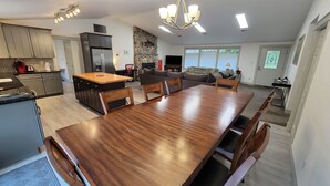 Une cuisine moderne avec un îlot central, un coin repas doté d’une grande table en bois et un salon avec un canapé et un téléviseur.