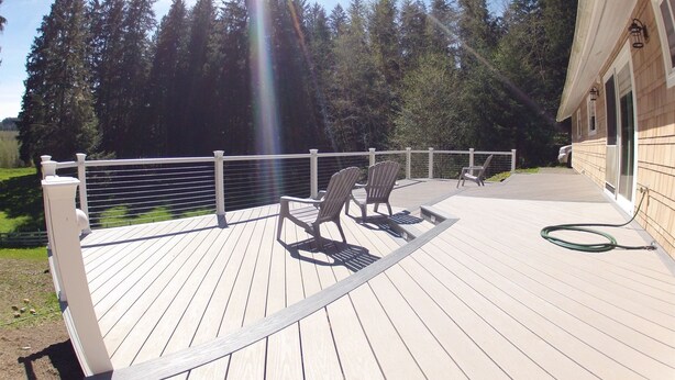 Une terrasse en bois avec une balustrade blanche, deux fauteuils Adirondack et un tuyau d’arrosage sur le côté droit.