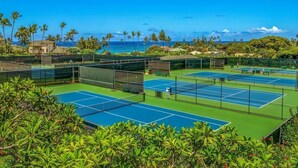 A tennis court complex with multiple courts, surrounded by lush greenery and overlooking a beach. - Ocean View & AC! 3 Min Walk To Poipu Beach! (Koloa)
