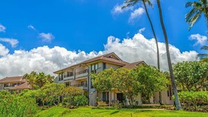 A two-story building with a balcony, surrounded by lush greenery and palm trees. - Ocean View & AC! 3 Min Walk To Poipu Beach! (Koloa)