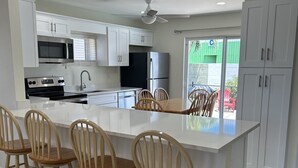 Une cuisine moderne avec des meubles blancs, un îlot central doté de tabourets, des appareils en acier inoxydable et un ventilateur de plafond.