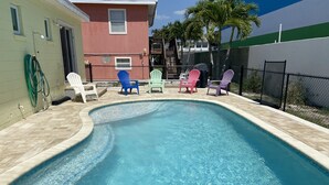 Une piscine à bordures courbes, entourée d’une terrasse carrelée. On y trouve des fauteuils Adirondack aux couleurs vives et un tuyau d’arrosage fixé au mur.