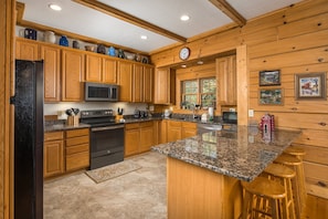 A kitchen with wooden cabinets, a granite countertop, a stainless steel refrigerator, and a microwave.