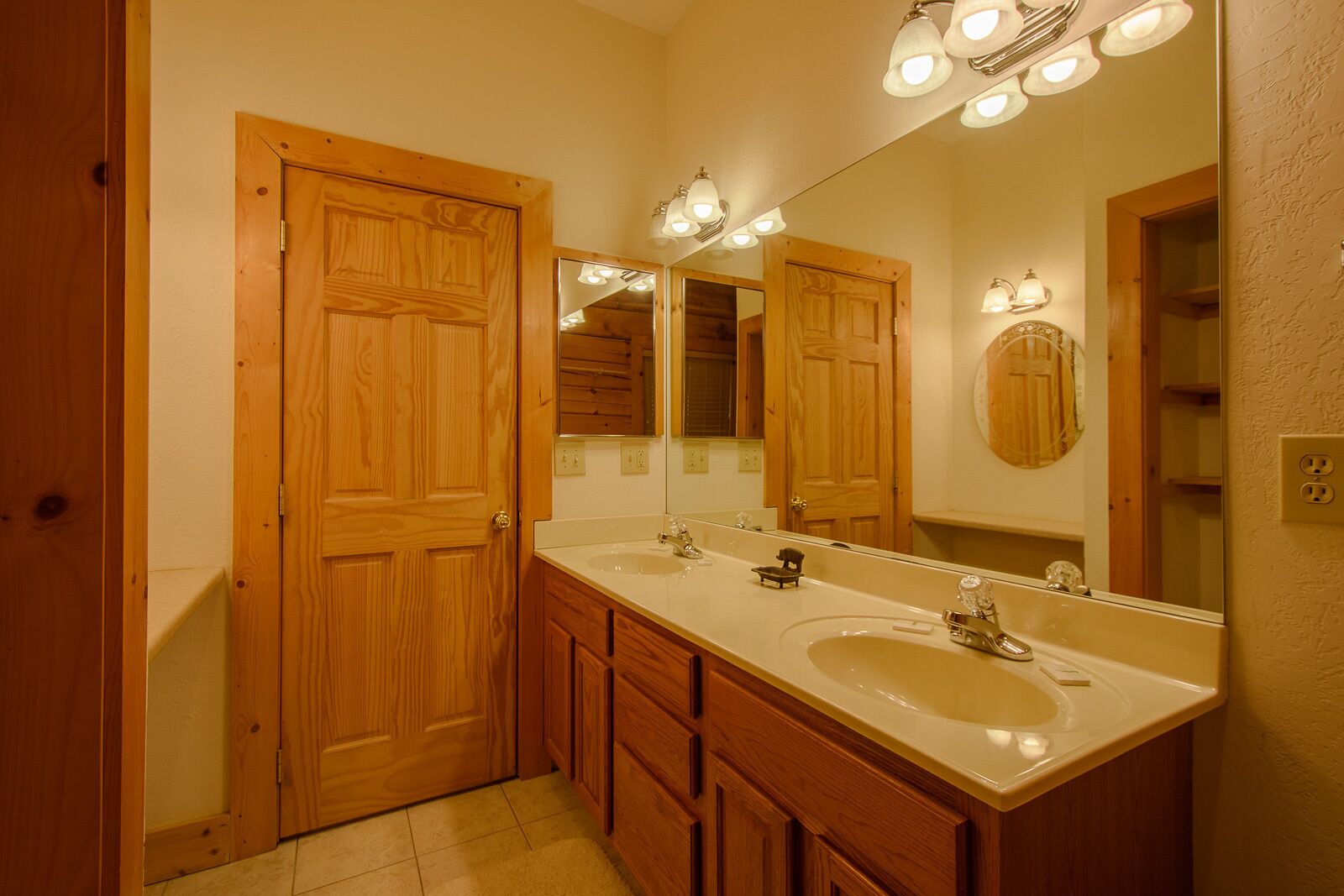 A bathroom with wooden doors, a double sink vanity, and a large mirror with lights above.