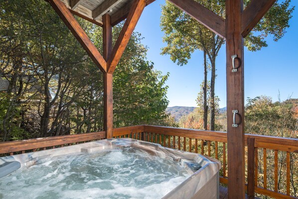 A hot tub in a wooden deck with a view of trees and hills.