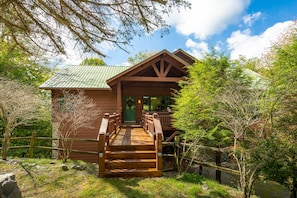 A wooden cabin with a porch, surrounded by trees and a clear sky.
