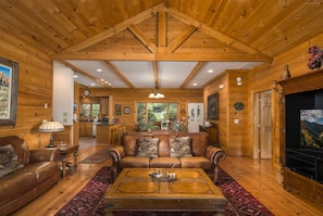 A spacious living room with a high ceiling, wooden walls, a leather sofa, a coffee table, and a television.