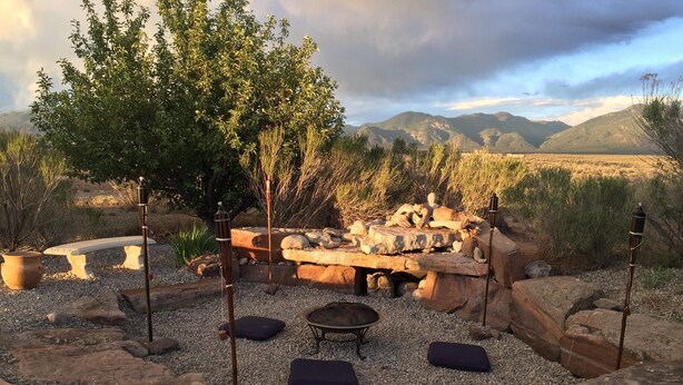 Un espacio al aire libre con una chimenea de piedra, bancos y vistas a las montañas.