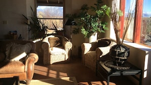 Un salón acogedor con muebles de mimbre, un ventanal con vistas a montañas y varias plantas en macetas.