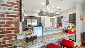 Una cocina moderna con encimeras de granito, una pared de acento de ladrillo y taburetes de bar rojos.