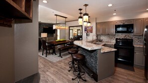 A modern kitchen with a central island, bar stools, a dining area with a wooden table and chairs, and built-in appliances. - Remodeled Penthouse - Ski In/Out - Huge Decks/Views - Private Hot Tub/Sauna (Durango)