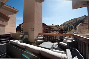 Een balkon met buitenmeubilair, een barbecue en uitzicht op een berg en gebouwen.