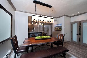 Een eetgedeelte met een houten tafel en banken, een hanglamp en een keuken op de achtergrond.