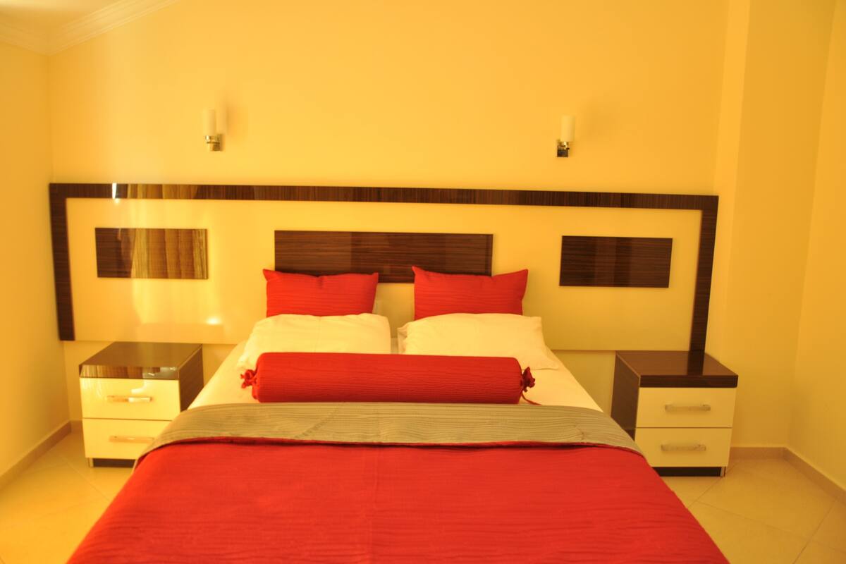 A hotel room with a large bed, two bedside tables, and a headboard with decorative panels.