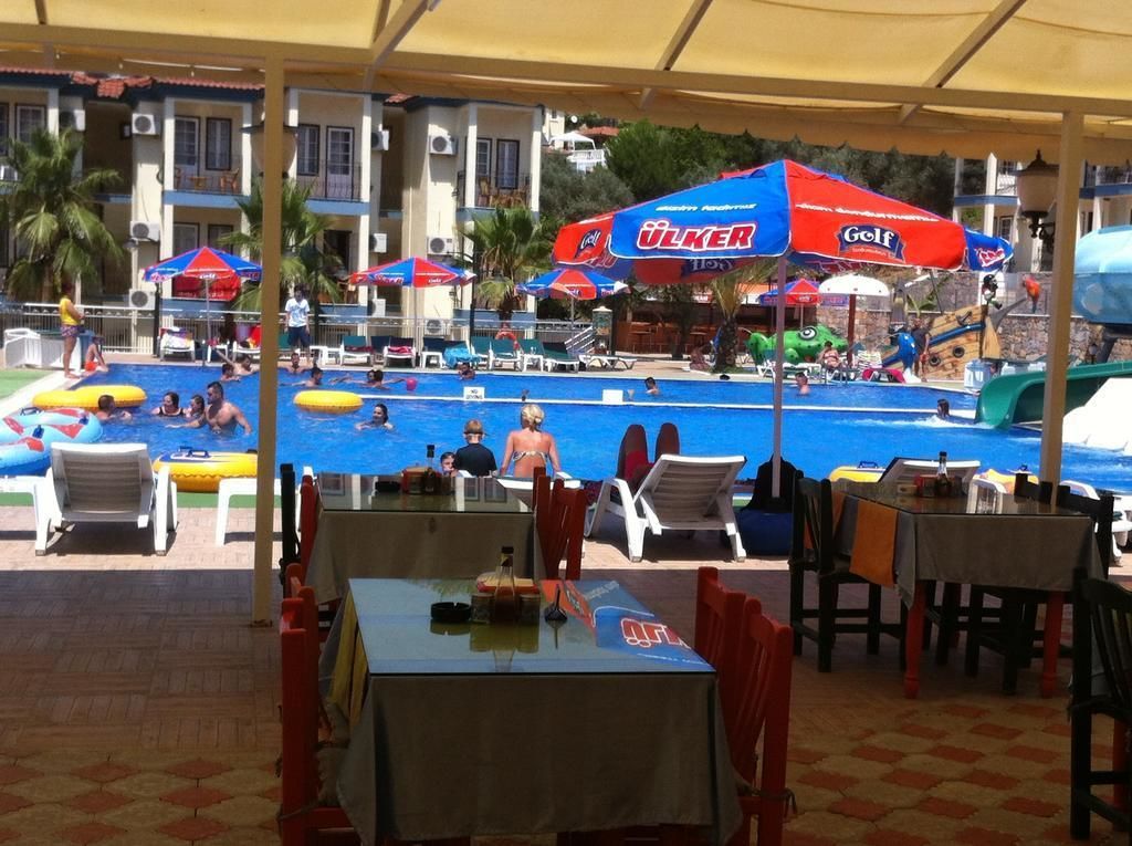 Un espace piscine doté de plusieurs parasols, de chaises longues et de tables, le tout installé sous une tonnelle.
