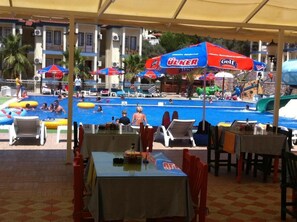 A pool area with multiple umbrellas, lounge chairs, and tables under a canopy. - Gurol Hotel & Apart (Fethiye)