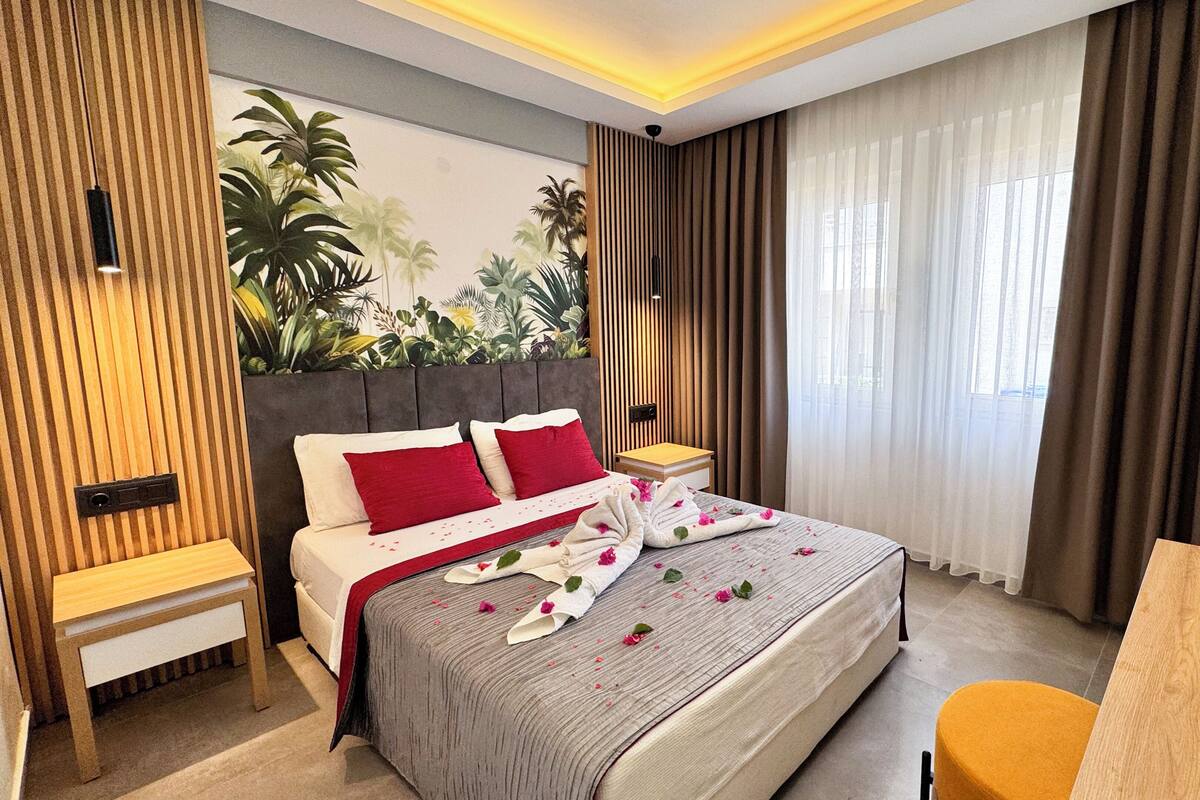A modern hotel room with a bed, bedside tables, a desk, and a large window with curtains.