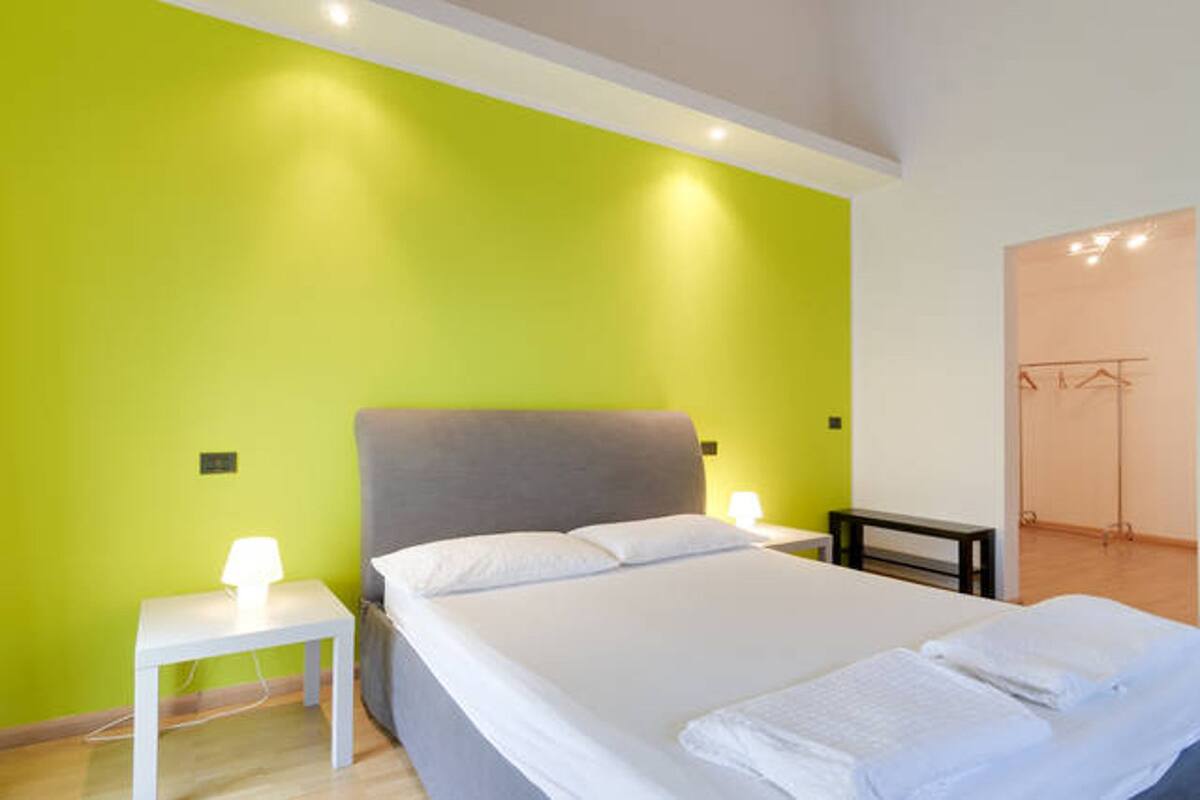 A bedroom with a bed, a nightstand, a lamp, and a wardrobe.
