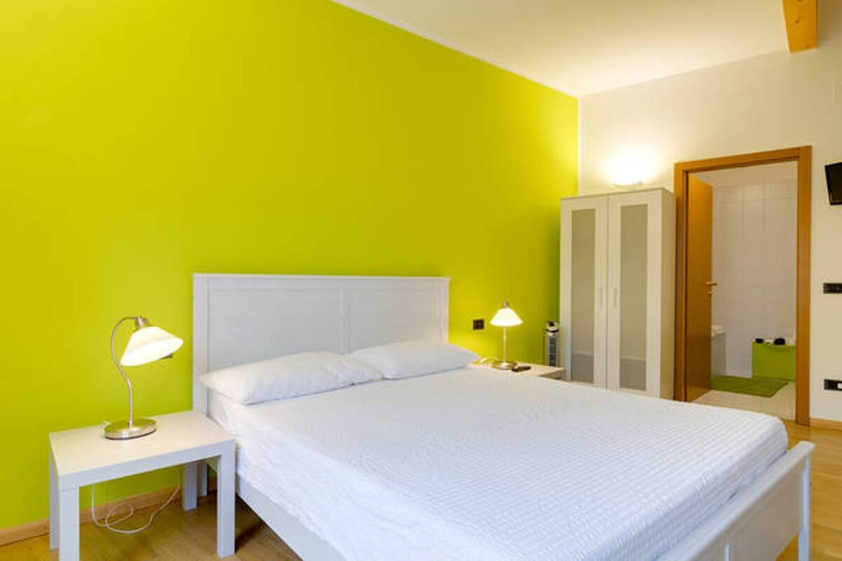 A bedroom with a white bed, two bedside lamps, a white nightstand, and a green wall.