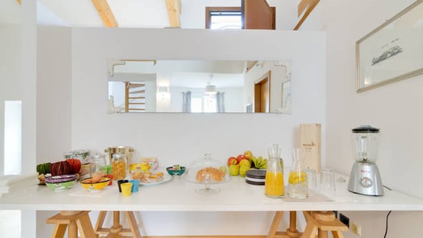 Une cuisine avec un plan de travail blanc, des tabourets en bois, un mixeur et divers aliments.