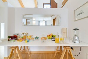 Eine Küche mit weißer Arbeitsplatte, Holzstühlen, einem Mixer und verschiedenen Lebensmitteln.