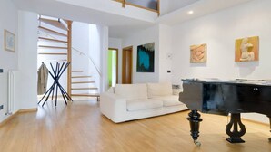 Un vaste espace de vie comprenant un canapé blanc, un piano noir et un escalier menant à un niveau supérieur.