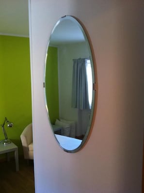 Een kamer met een ronde spiegel aan de muur, een klein tafeltje met een lamp en een groene muur.