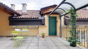 Une petite terrasse extérieure avec une table et des chaises, une porte verte et un pot de fleurs.