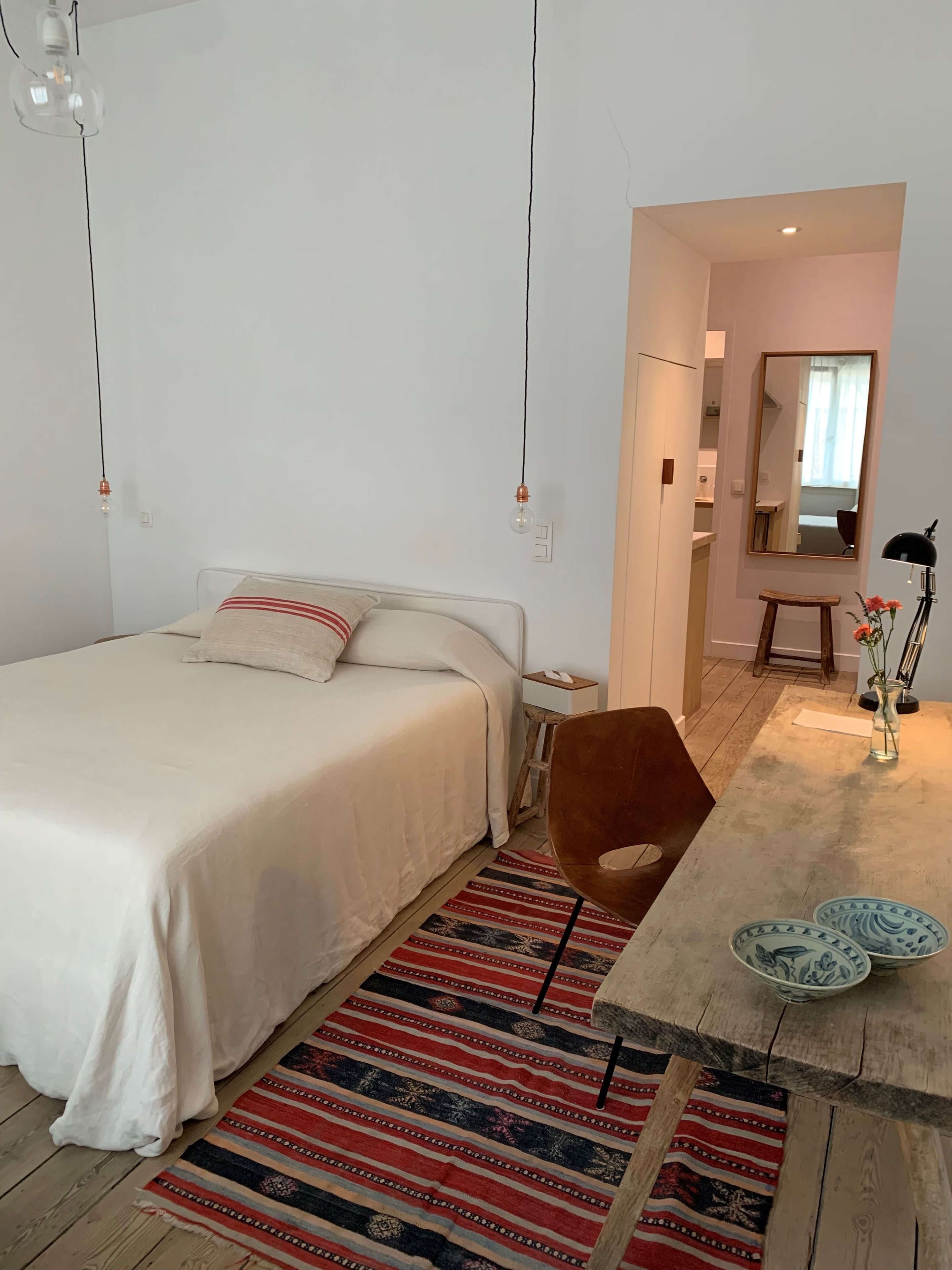 A bedroom with a bed, a chair, a desk, and a mirror.
