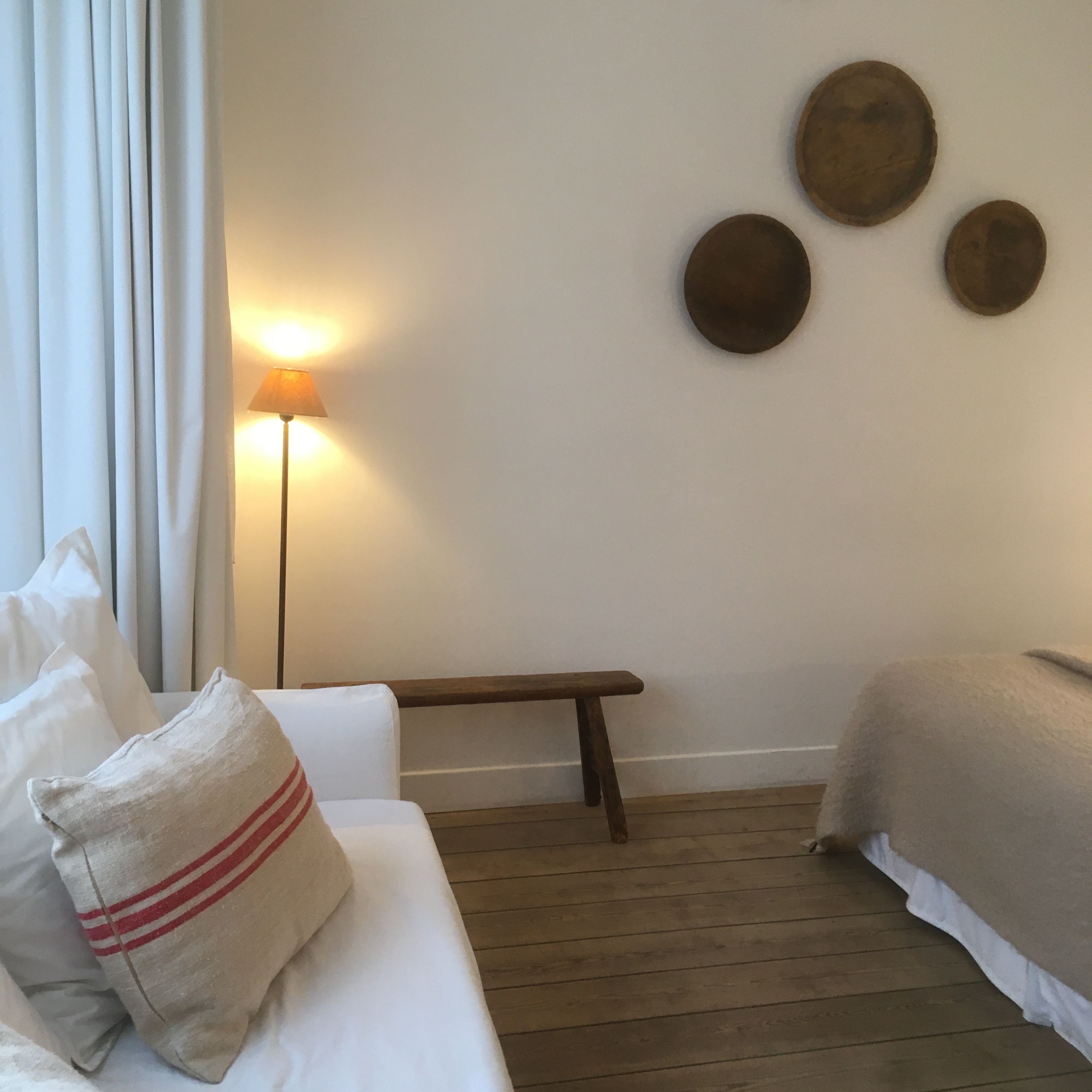 Habitación de hotel con cama, un banco, una lámpara y tres espejos redondos en la pared.