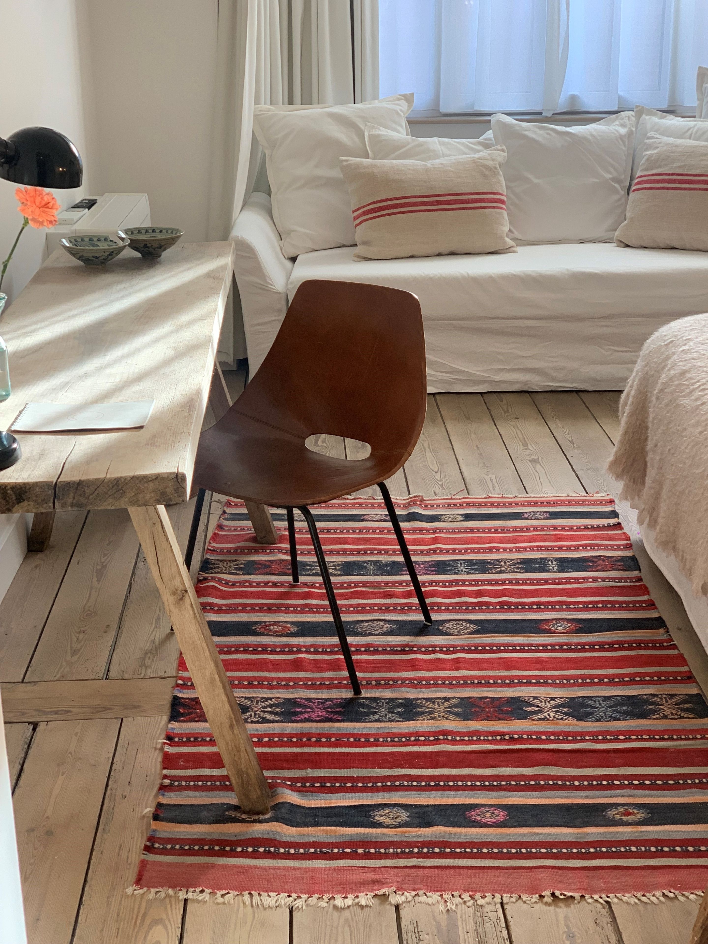 Un dormitorio con cama, escritorio y silla, ventana con cortinas y alfombra estampada.