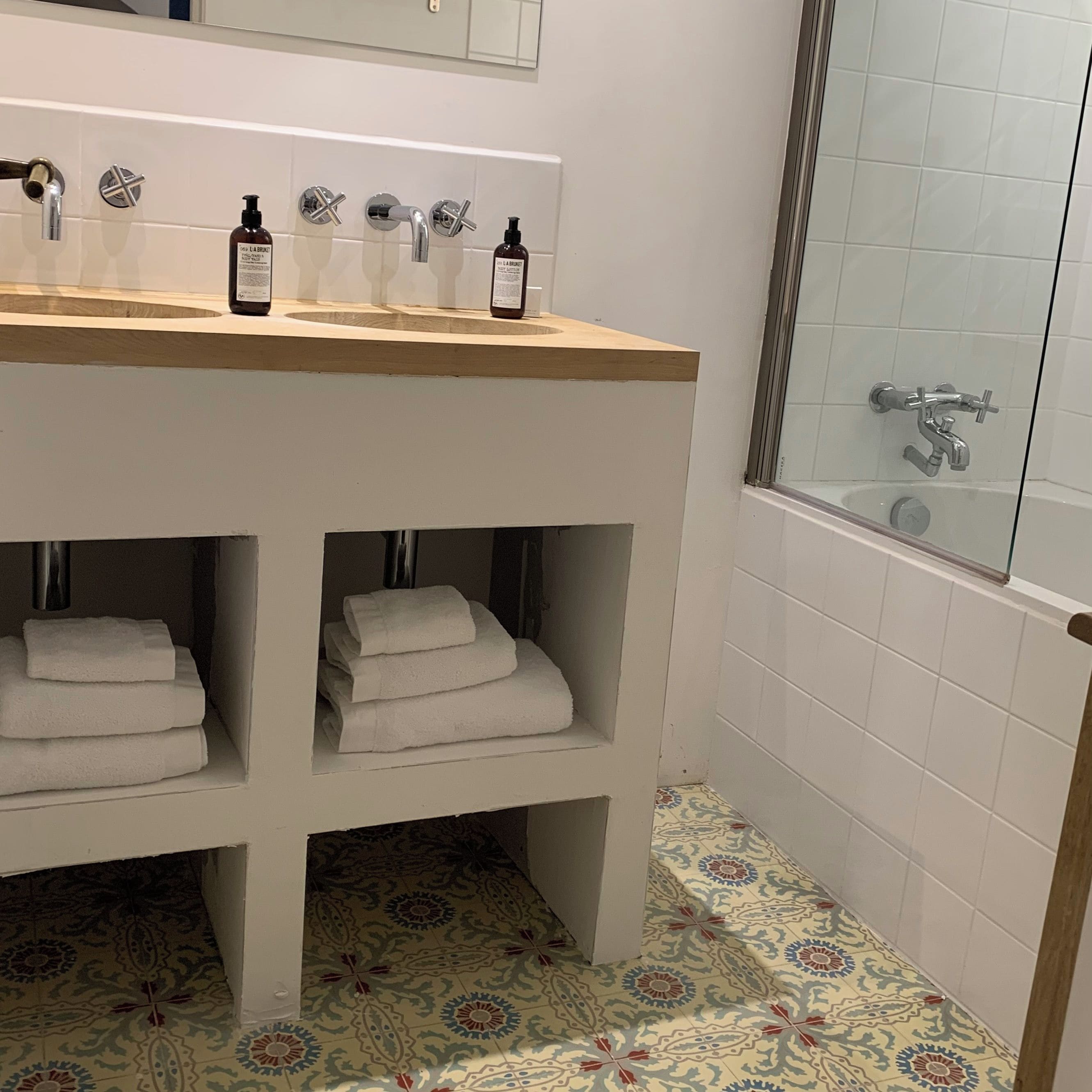Un baño con tocador de madera, cabina de ducha de vidrio y baldosas de piso estampadas.