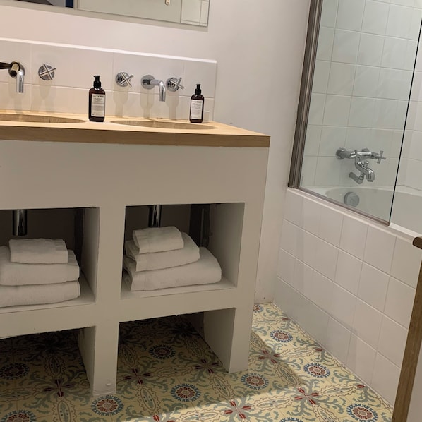 Un baño con tocador de madera, cabina de ducha de vidrio y baldosas de piso estampadas.