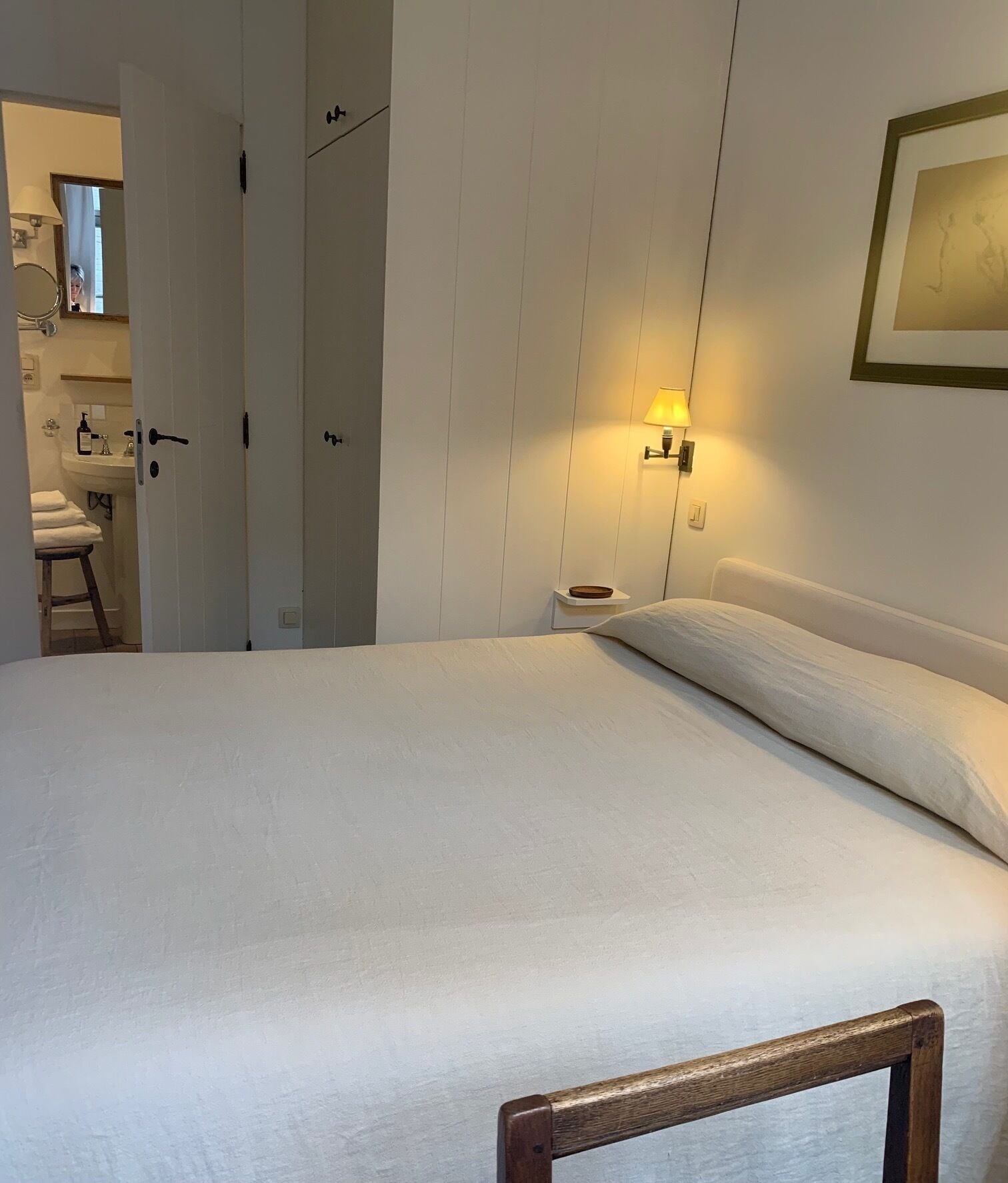 Camera d'albergo con un letto grande, un comodino, una lampada a parete e un bagno visibile attraverso una porta aperta.