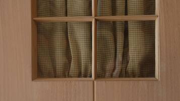 A wooden door with a window divided into six panes, each with a checkered curtain. The word "Toilet" is written below the window.