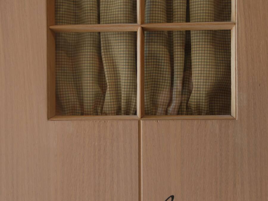A wooden door with a window divided into six panes, each with a checkered curtain. The word "Toilet" is written below the window.