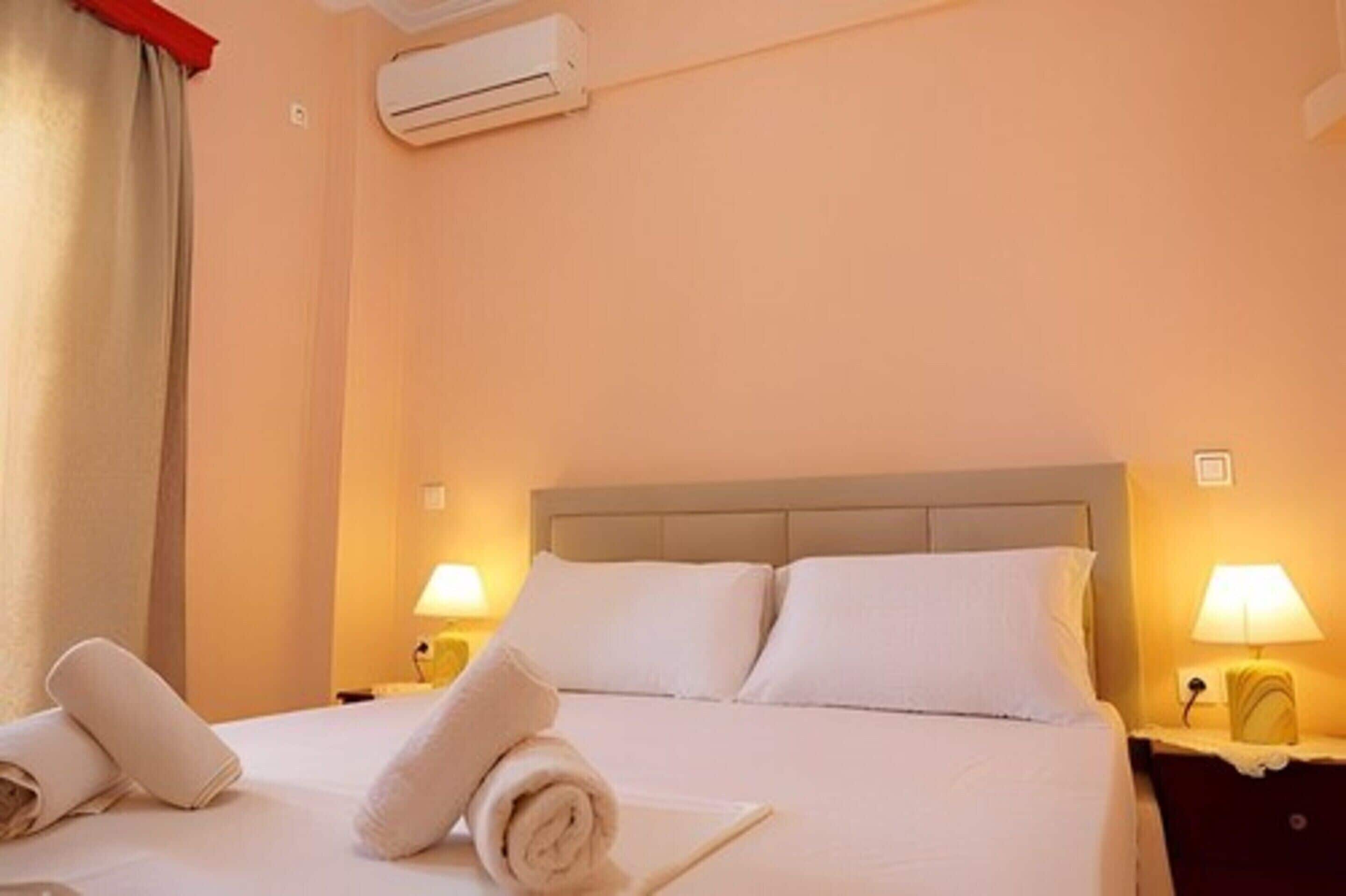 A hotel room with a bed, two bedside lamps, and an air conditioning unit.