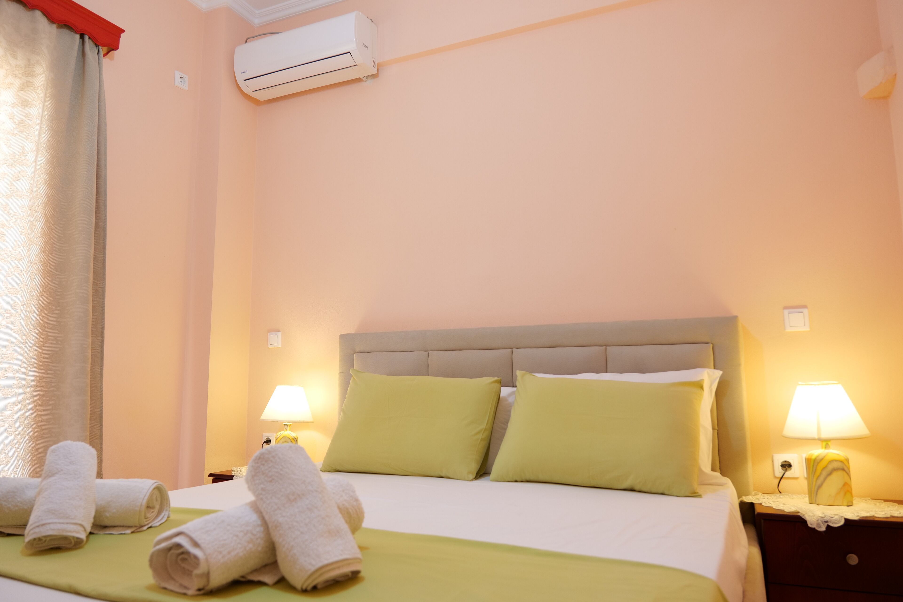Habitació d'hotel amb un llit, almoinades verdes, dues làmpades de nit i tovalloles arremolinades damunt el llit.