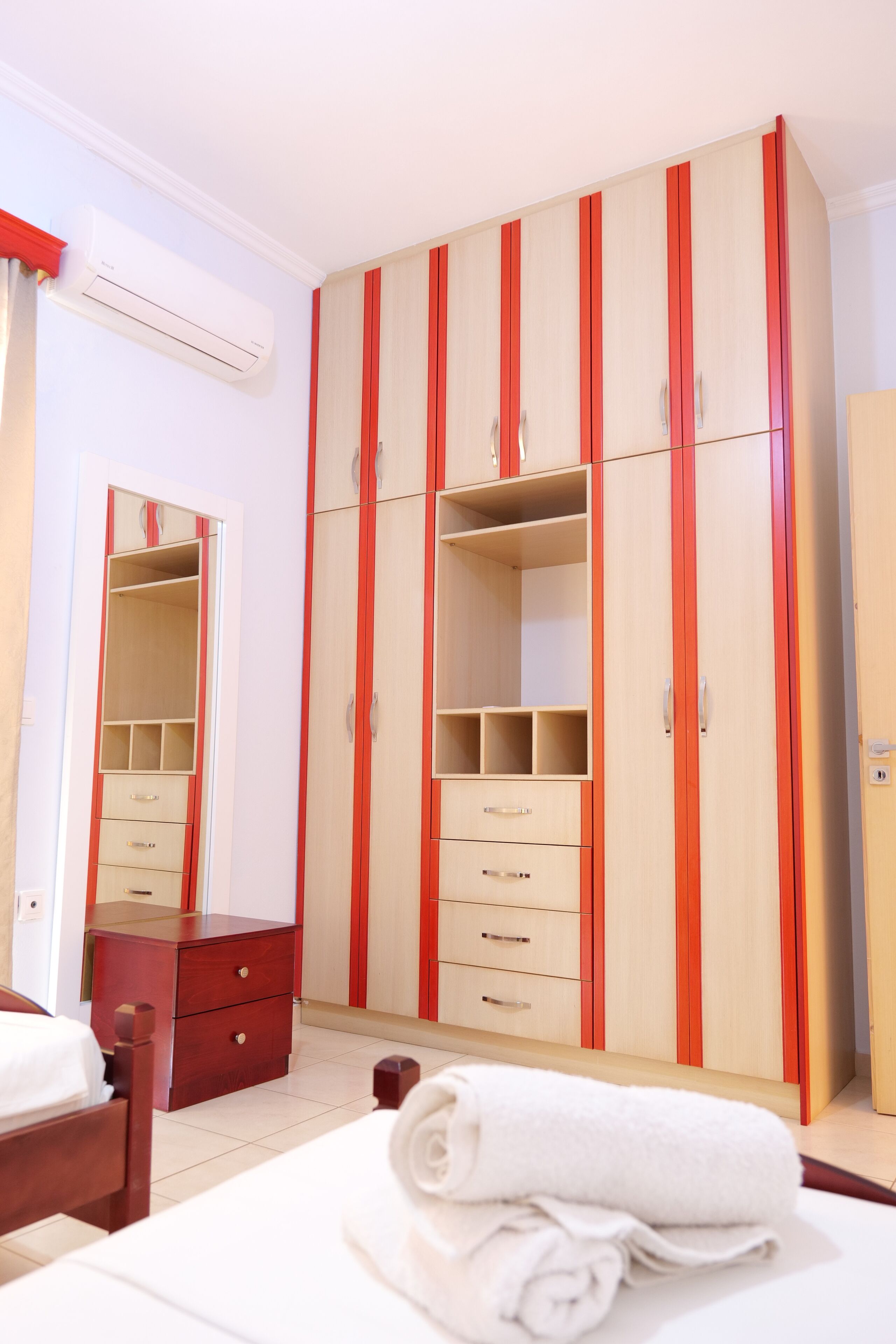 A bedroom with a large wardrobe, a mirror, a wooden nightstand, and a neatly made bed.