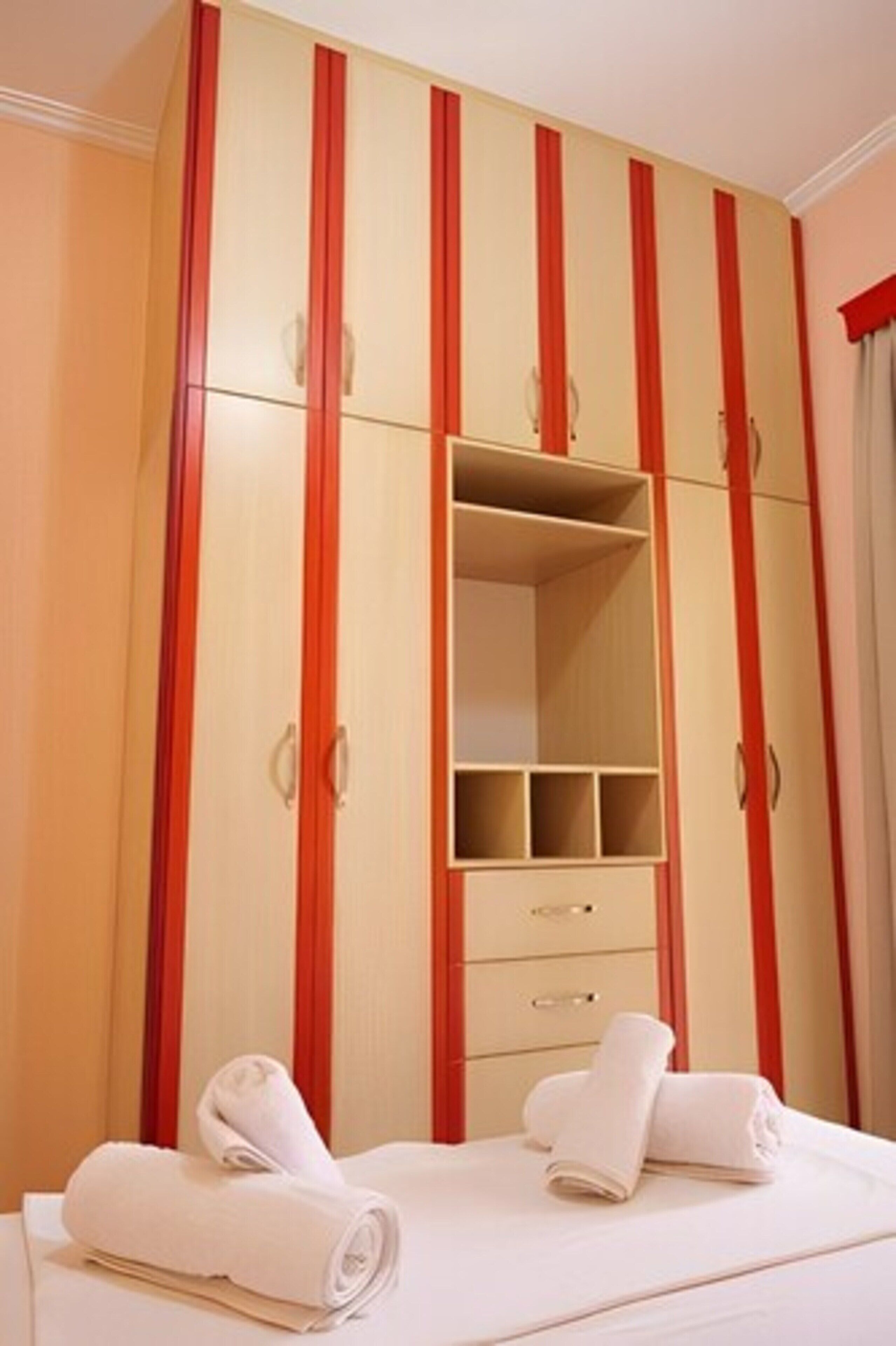 A bedroom with a large wardrobe, a bed, and two rolled towels on the bed.