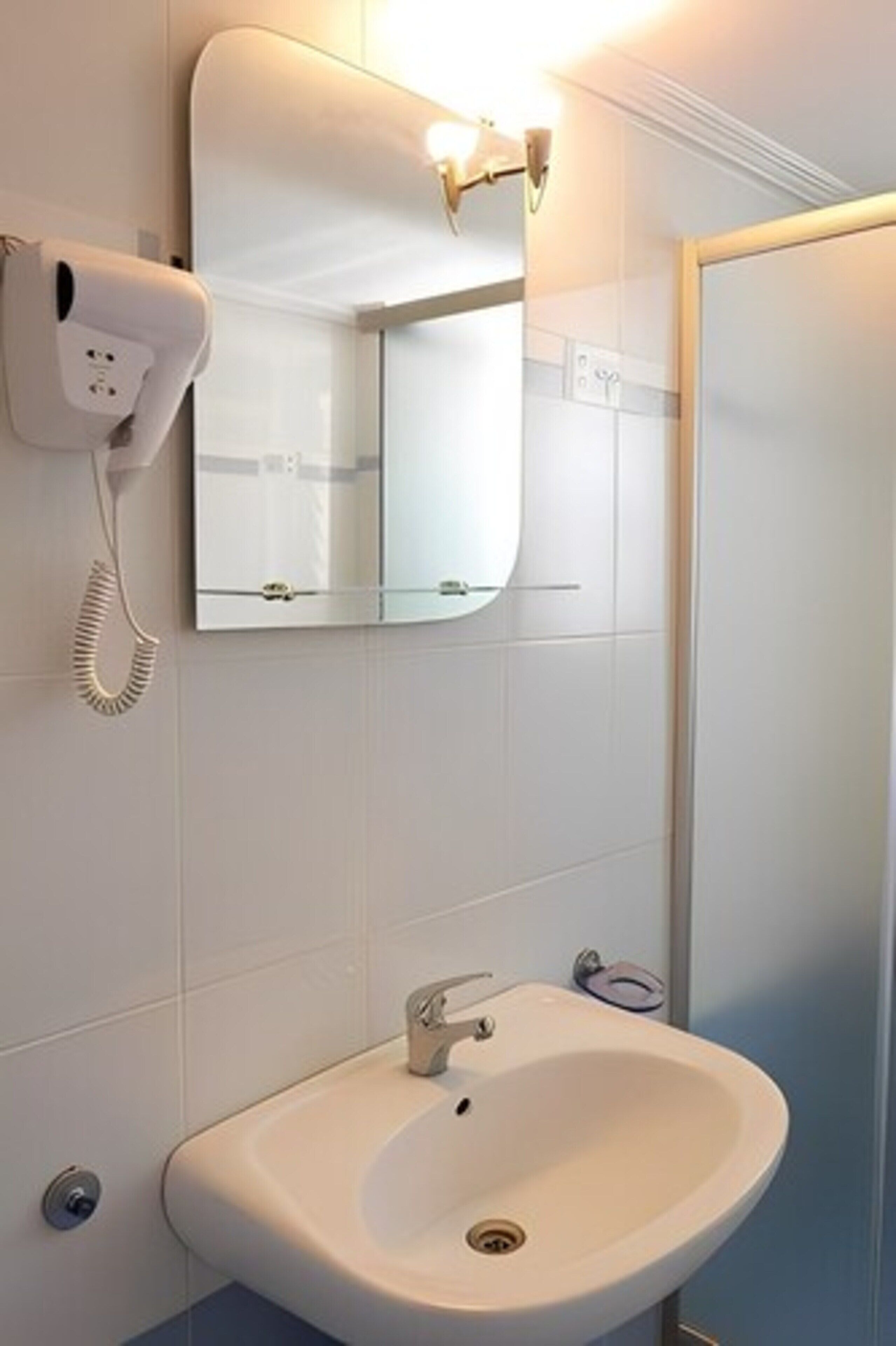 A bathroom with a white sink, a mirror, and a hairdryer on the wall.