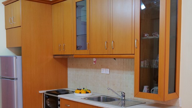 A compact kitchen with wooden cabinets, a built-in oven, a refrigerator, and a sink. - Miracle Luxury Apartments (Sarandë)